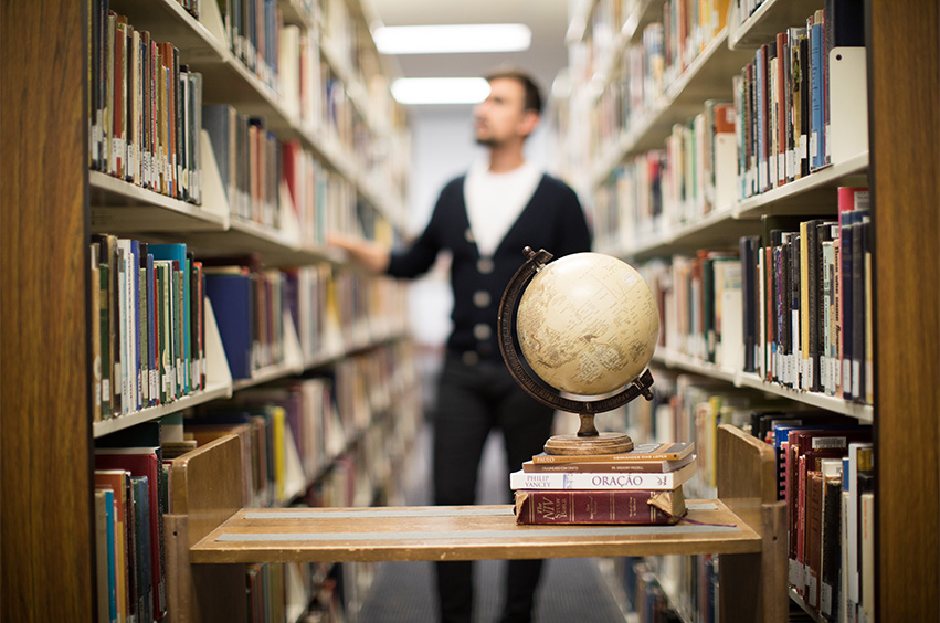 dallas college student looking at bookshelves in library with globe in foreground